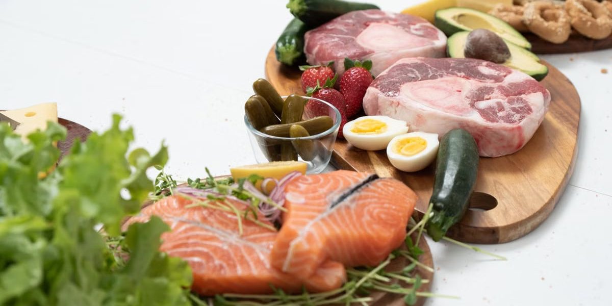 Assorted fresh keto ingredients including salmon, beef, and vegetables on wooden boards, perfect for healthy meals.