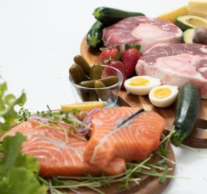 Assorted fresh keto ingredients including salmon, beef, and vegetables on wooden boards, perfect for healthy meals.