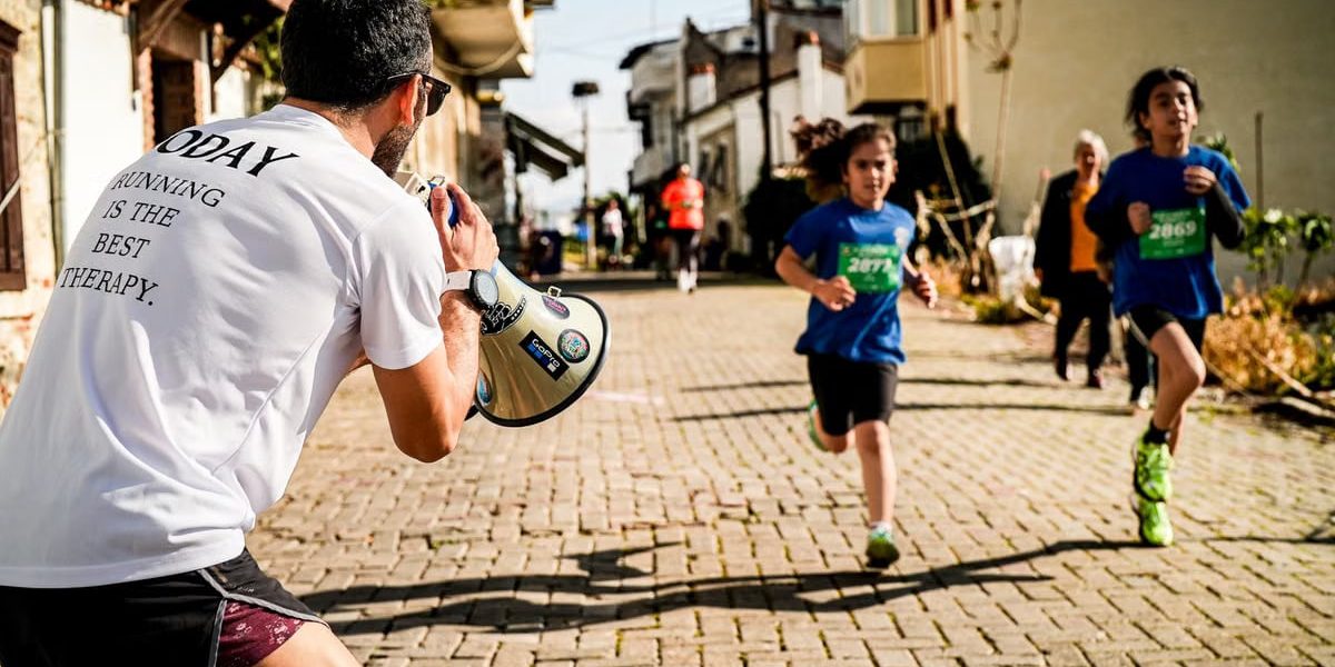 Children running a street race while a man with a megaphone cheers them on.