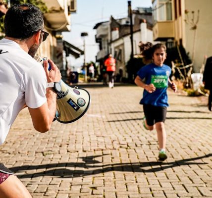 Children running a street race while a man with a megaphone cheers them on.